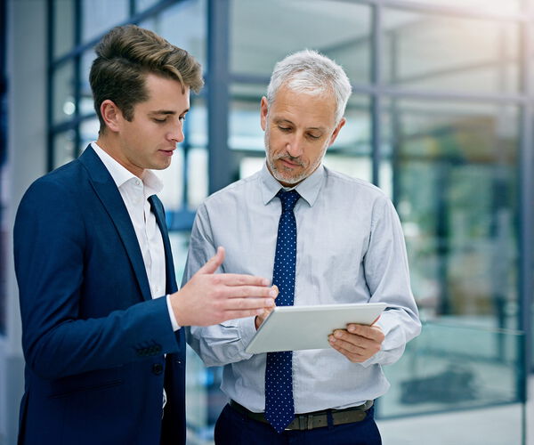 Professionelles Beratungsgespräch in moderner Büroumgebung Zwei Geschäftsmänner im Gespräch in einem modernen Bürogebäude, einer zeigt dem anderen etwas auf einem Tablet.