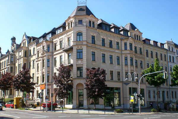 Stilvolles Altbaugebäude an belebter Kreuzung Historisches Mehrfamilienhaus mit Geschäften im Erdgeschoss an einer Straßenecke in einer europäischen Stadt bei sonnigem Wetter.
