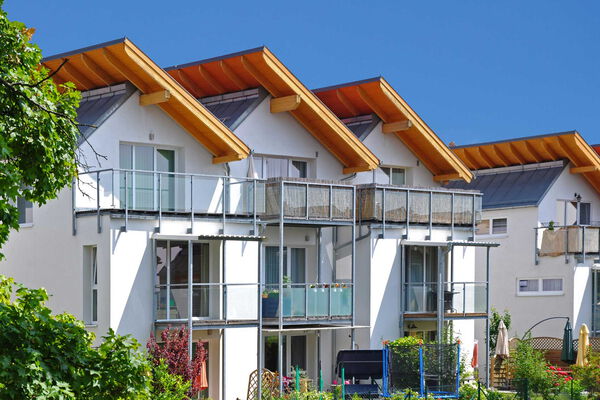 Familienfreundliche Reihenhäuser mit Balkon und Garten Reihenhäuser mit markanten Satteldächern, Holzelementen und Balkonen in einer grünen Wohnsiedlung bei sonnigem Wetter.
